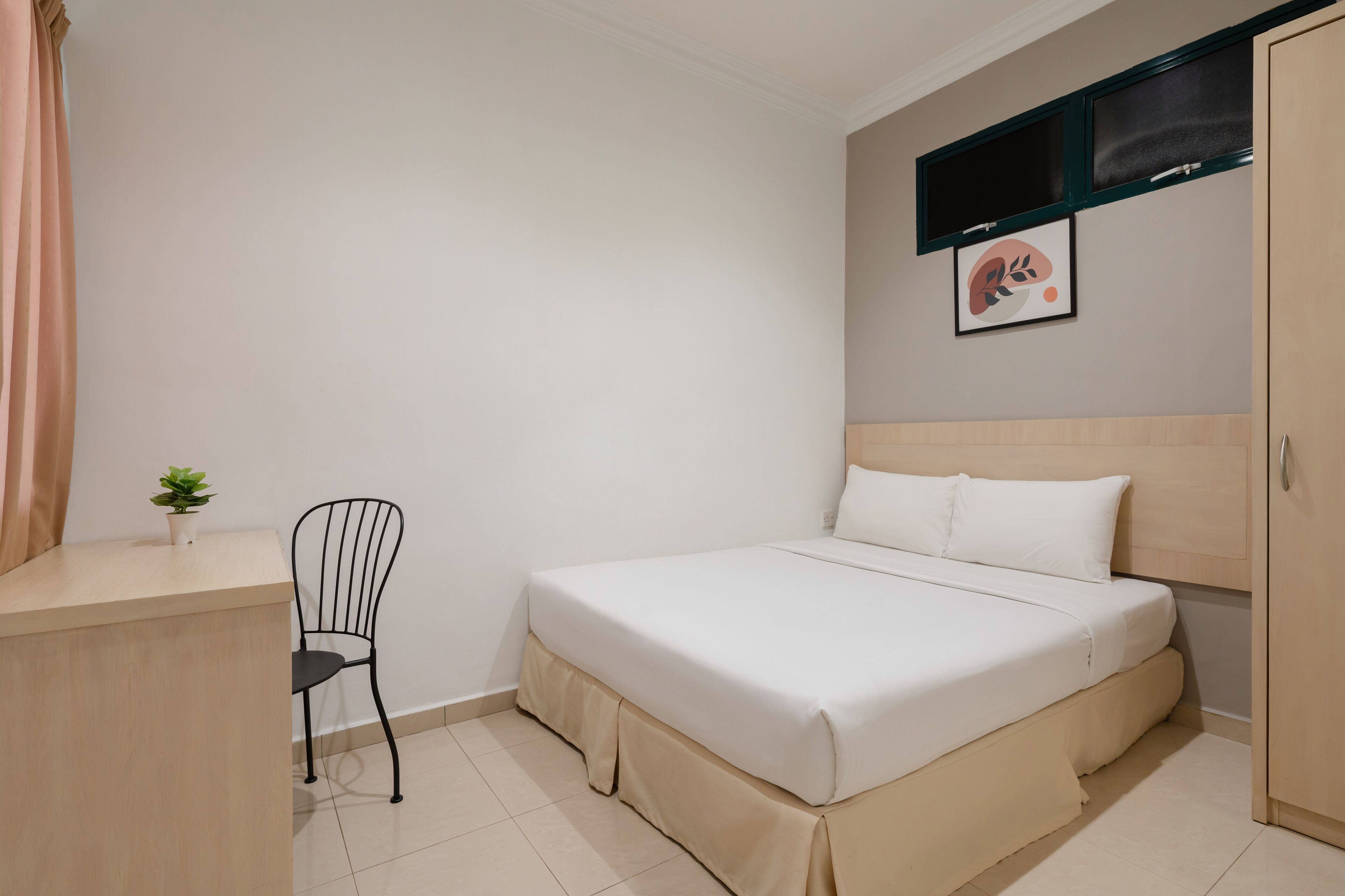 Un dormitorio con cama, escritorio, silla, planta en maceta y televisor instalado en la pared.