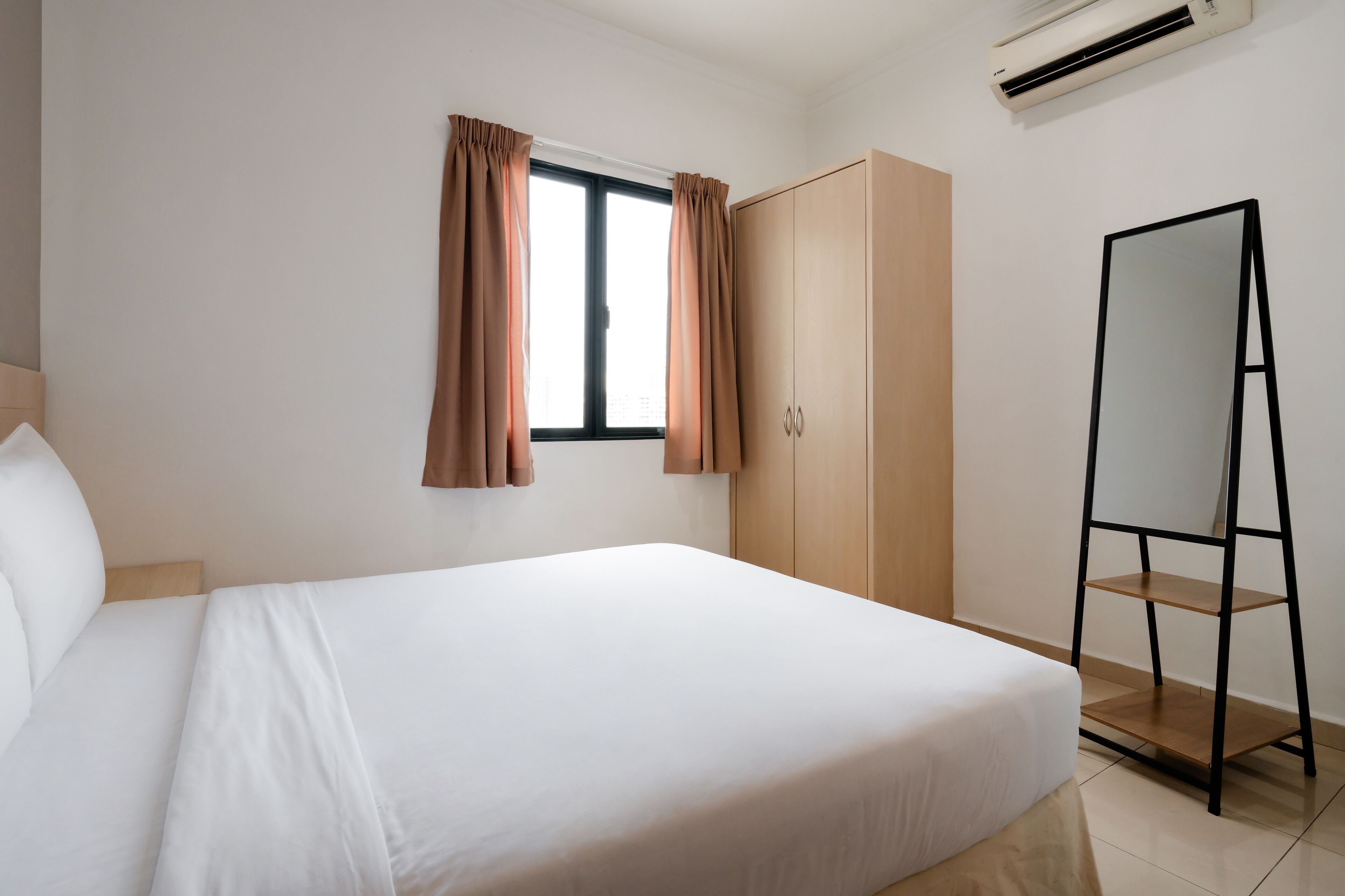 Une chambre d’hôtel avec un lit, une armoire, un miroir et une fenêtre avec des rideaux.