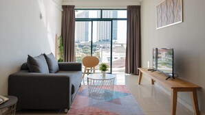 A modern living room with a sofa, a round coffee table, a TV on a wooden stand, and a large window with curtains. - Golden View Serviced Apartment (George Town)
