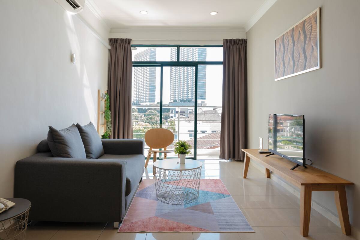 A modern living room with a sofa, a round coffee table, a TV on a wooden stand, and a large window with curtains.