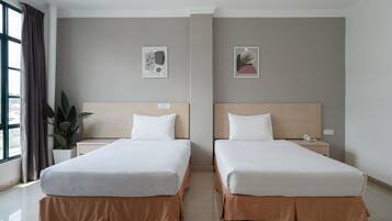A hotel room with two beds, a potted plant, and artwork on the walls.