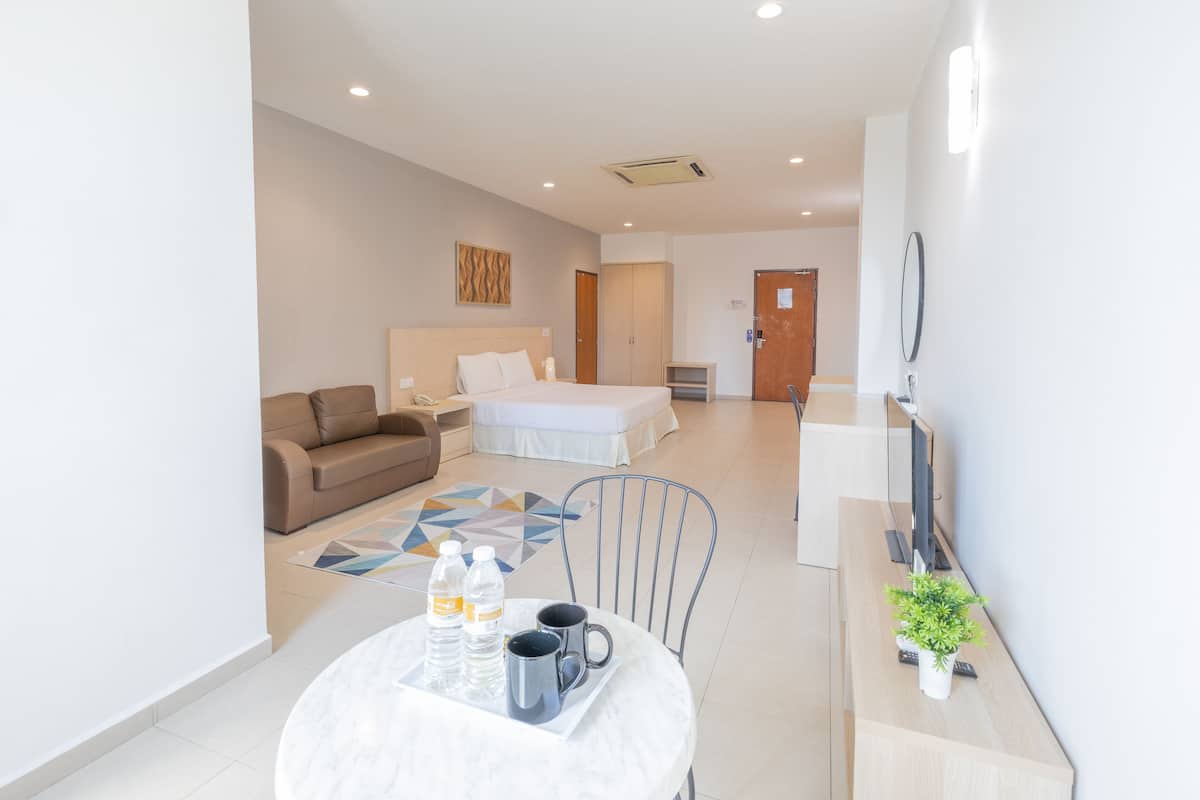 A modern hotel room with a bed, a sofa, a dining table with water bottles and a tray, and a TV on a wooden desk.