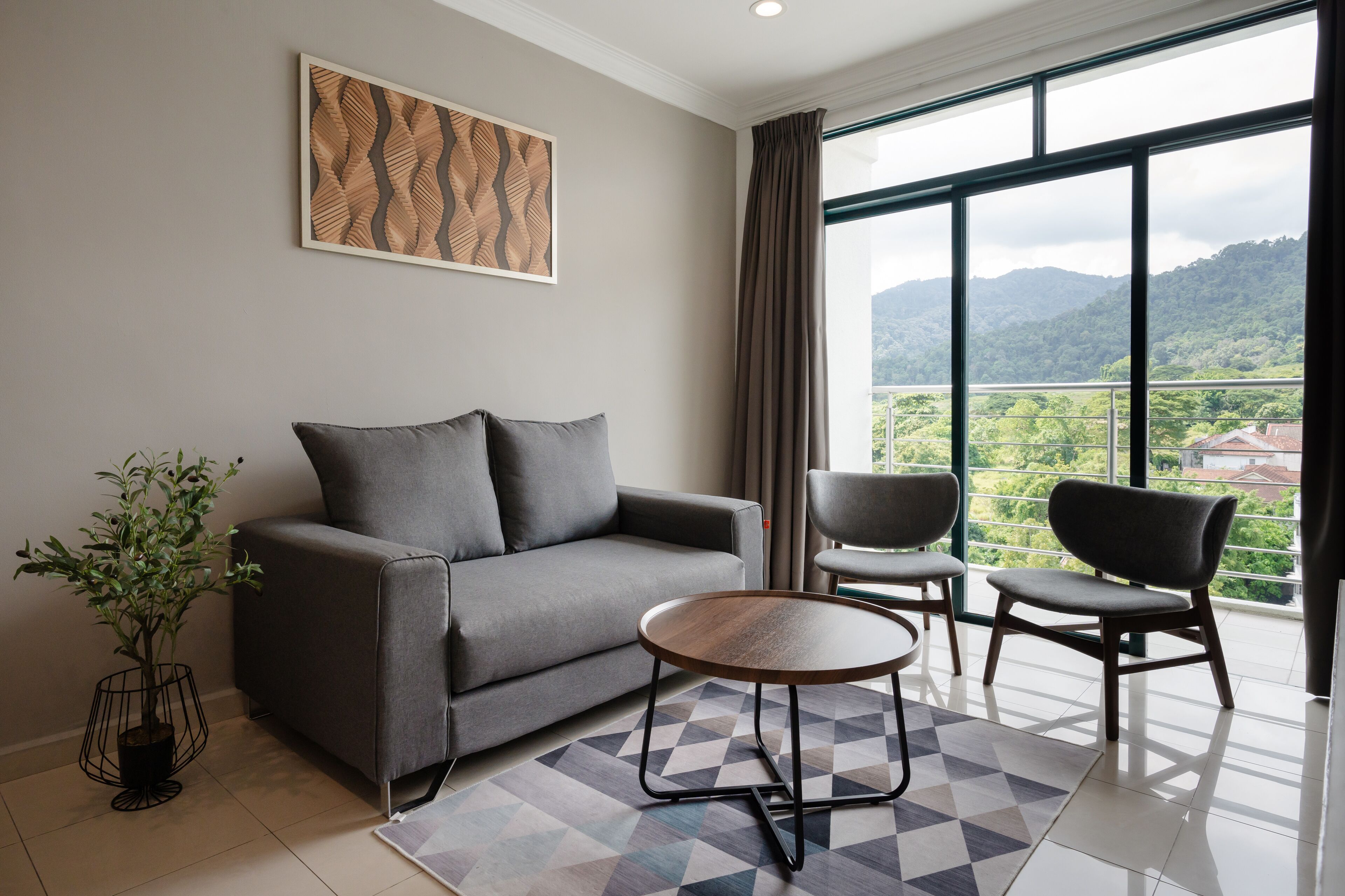 A modern living room with a grey sofa, two armchairs, a round coffee table, and a large window offering a view of green hills.