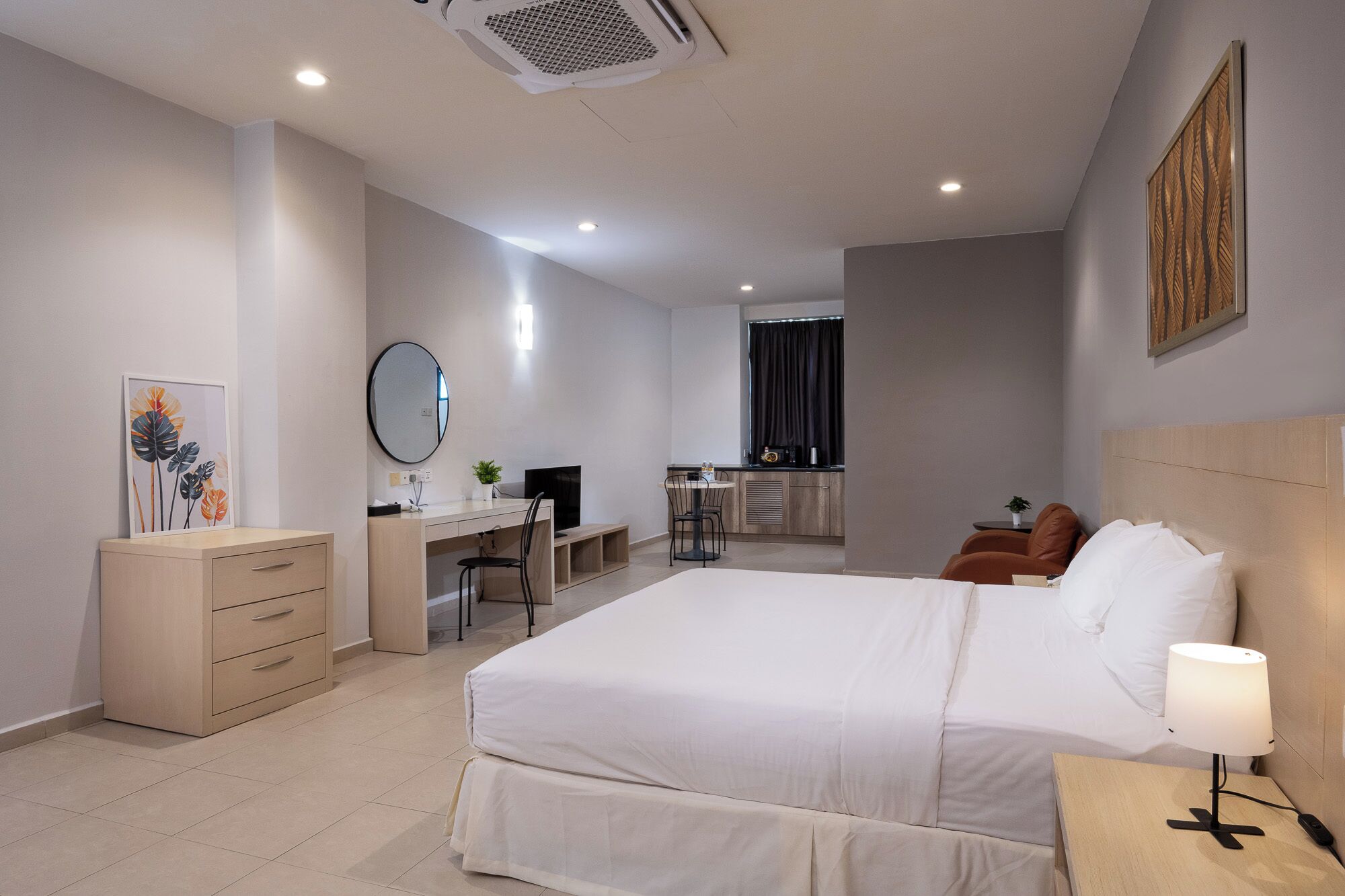 A hotel room with a bed, desk, chair, and a small kitchenette.