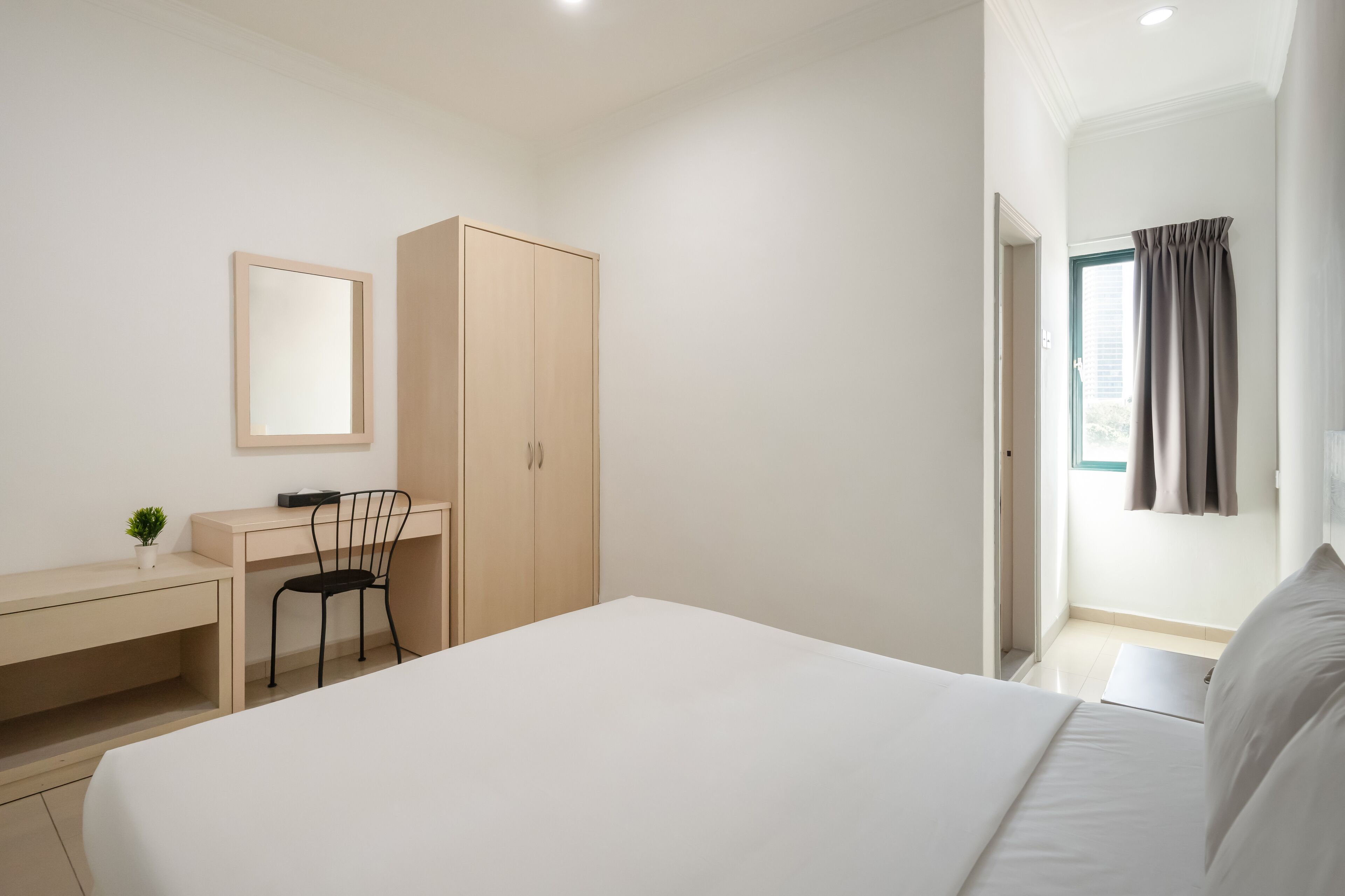 A bedroom with a bed, a desk, a chair, a wardrobe, and a window with curtains.