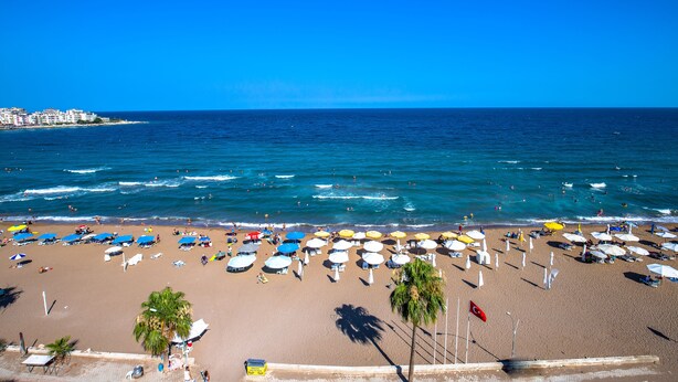 A beach with rows of umbrellas and sun loungers, a clear blue sky, and the ocean. - Süzer Resort Hotel (Silifke)