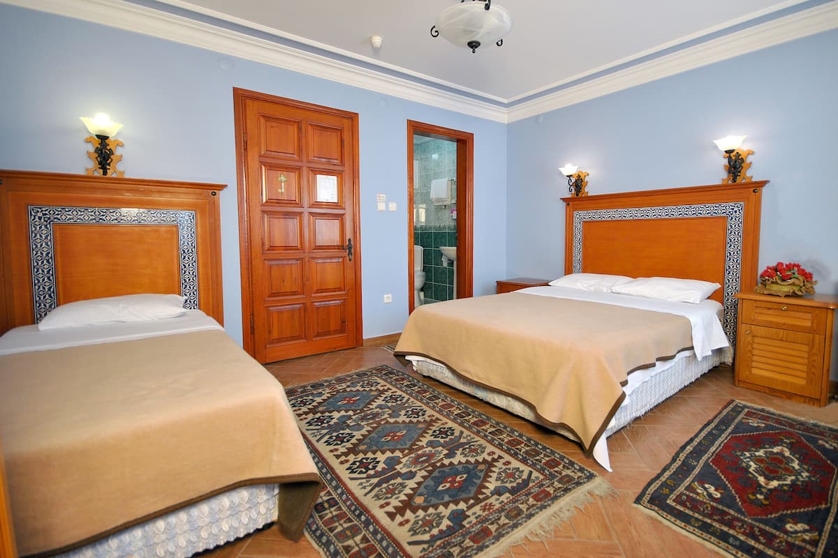 A hotel room with two beds, a wooden door, a bathroom, and a patterned rug.
