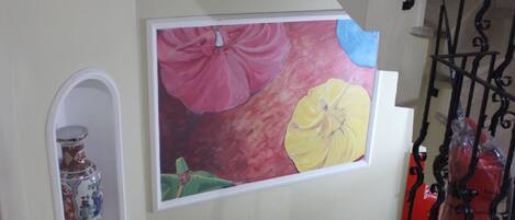 Una escalera con barandilla decorativa, un cuadro enmarco con flores y un jarrón en la pared.