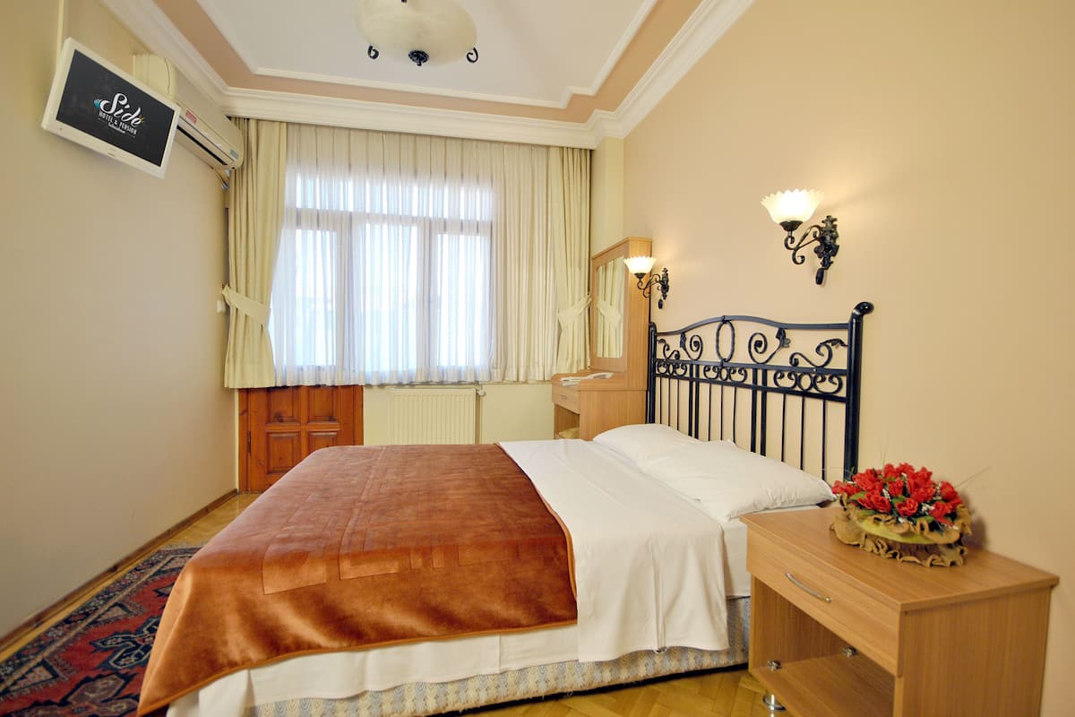 A hotel room with a bed, a nightstand, a lamp, a mirror, and a window with curtains.