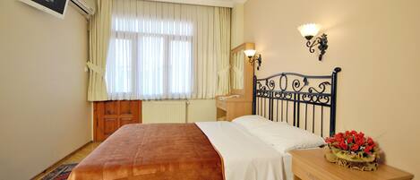 A hotel room with a bed, a nightstand, a lamp, a mirror, and a window with curtains.