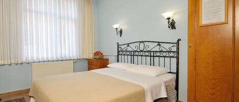 Une chambre à coucher avec un lit, une table de chevet, une porte en bois et une fenêtre avec des rideaux.
