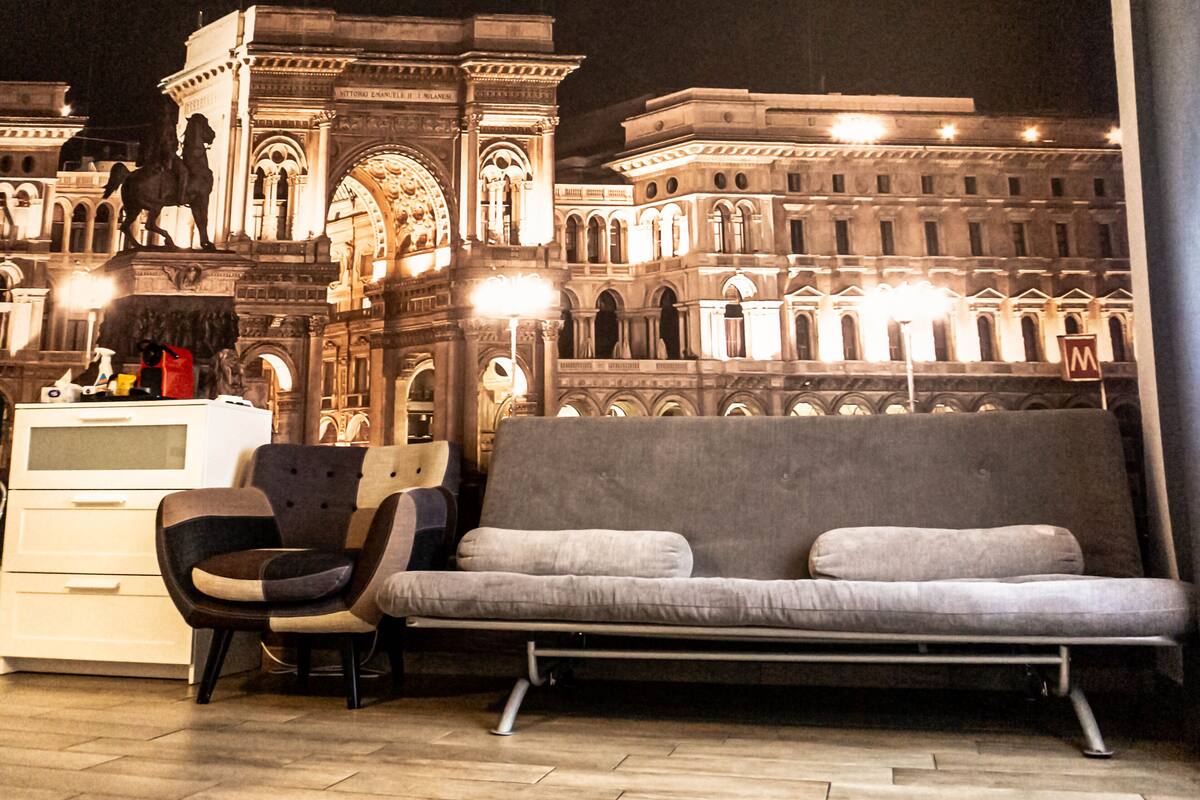 Un salon moderne avec un canapé et un fauteuil, une commode et une vue sur un bâtiment historique à l’architecture classique.