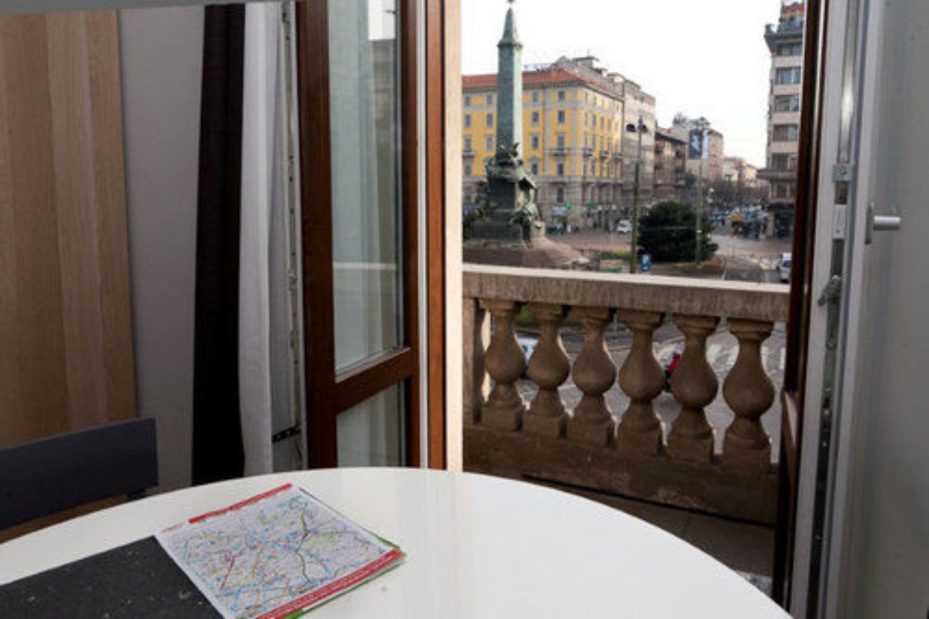 A room with a map on the table, a window with a view of a cityscape, and a balcony with a balustrade.