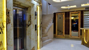A marble-floored lobby with an elevator, a staircase, and a reception desk.