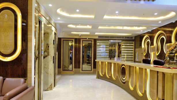 A modern hotel lobby with a curved reception desk, marble flooring, and a seating area with leather chairs.