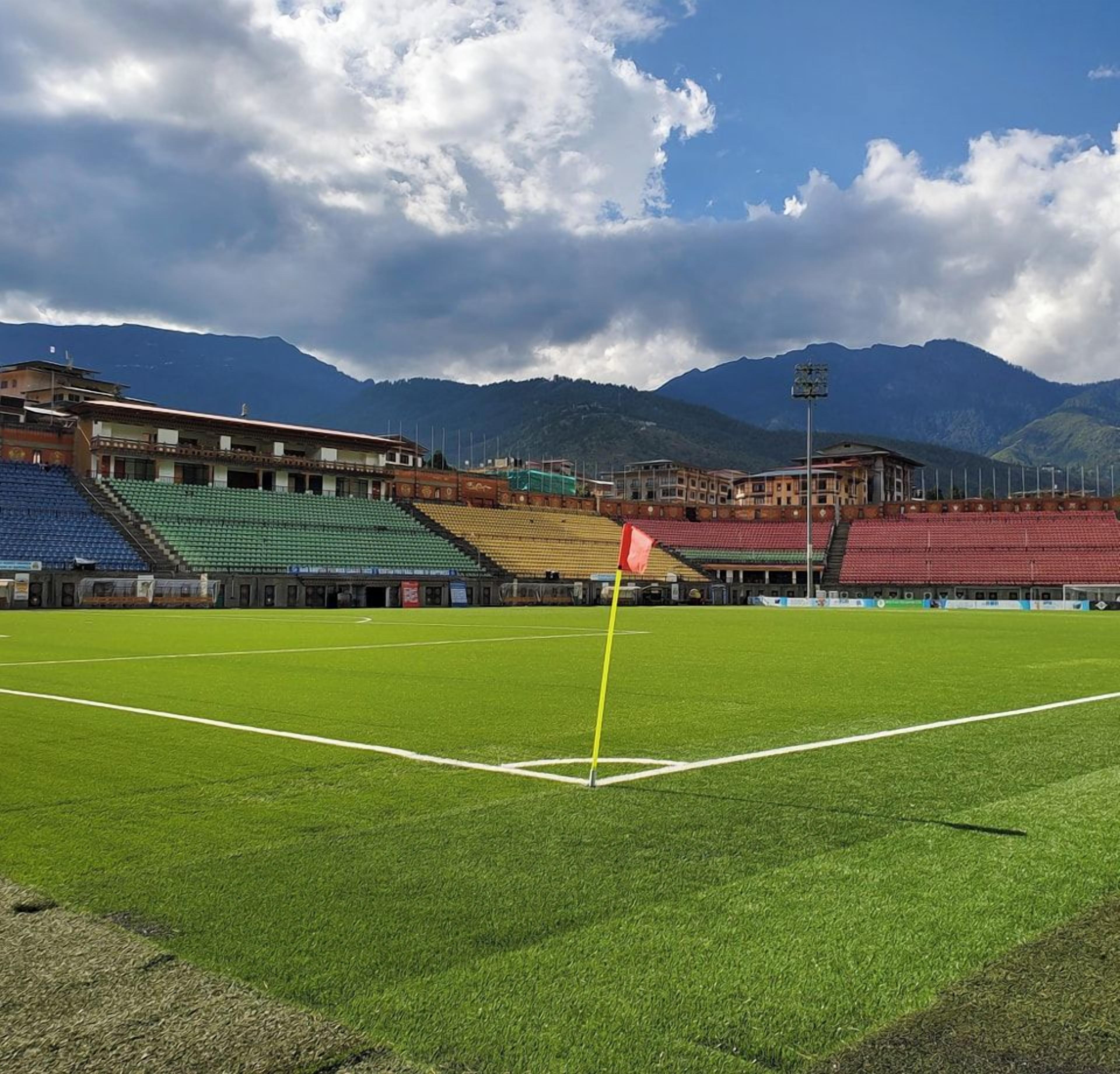 A stadium with tiered seating and a green field, surrounded by mountains.