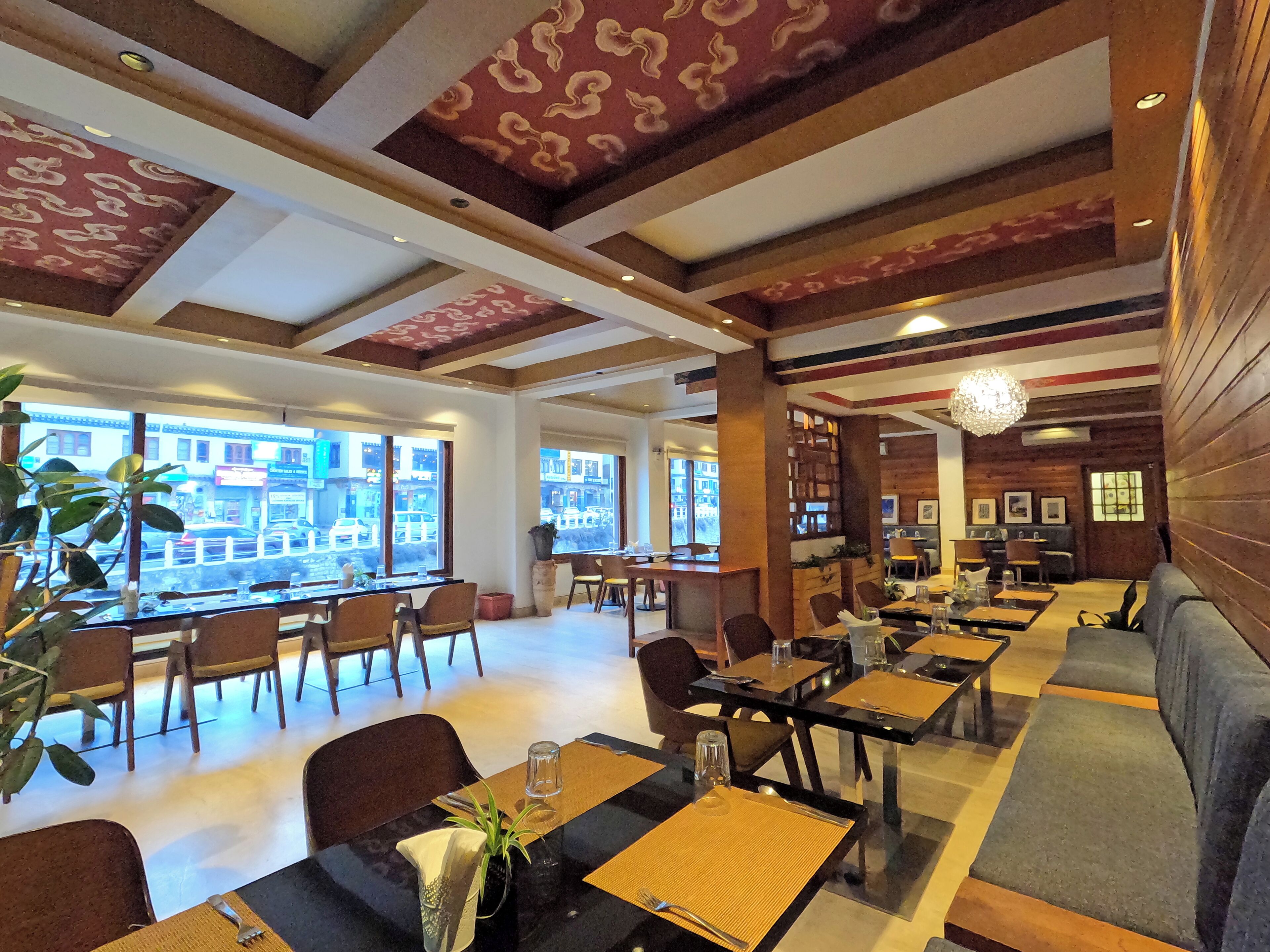 A restaurant with multiple dining tables and chairs, large windows with a view of the street, and a mix of wooden and modern decor.