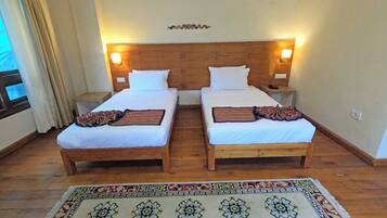 Quarto duplo com duas camas, cada uma com roupa de cama branca e um cobertor decorativo estampado. Há mesas de cabeceira com abajures e um objeto decorativo na parede, acima das camas.
