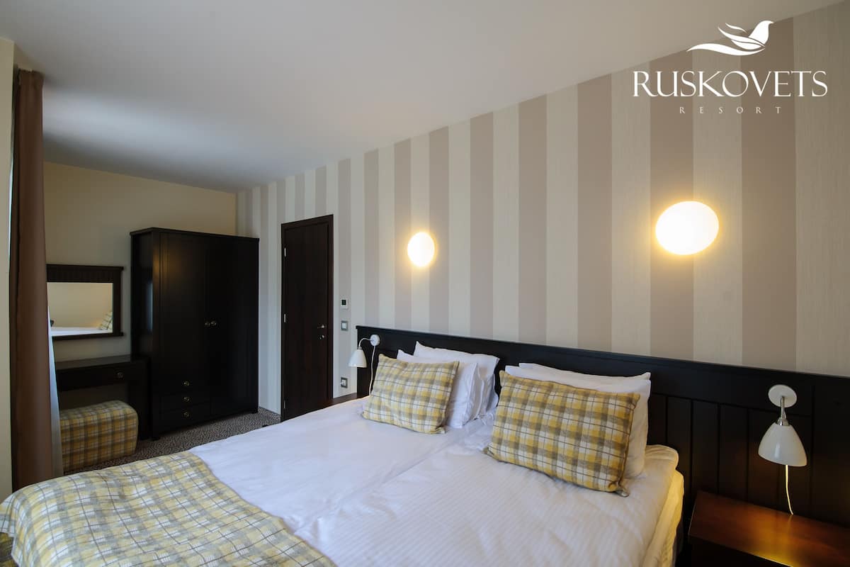 A hotel room with a large bed, two bedside tables, a wardrobe, and a mirror.