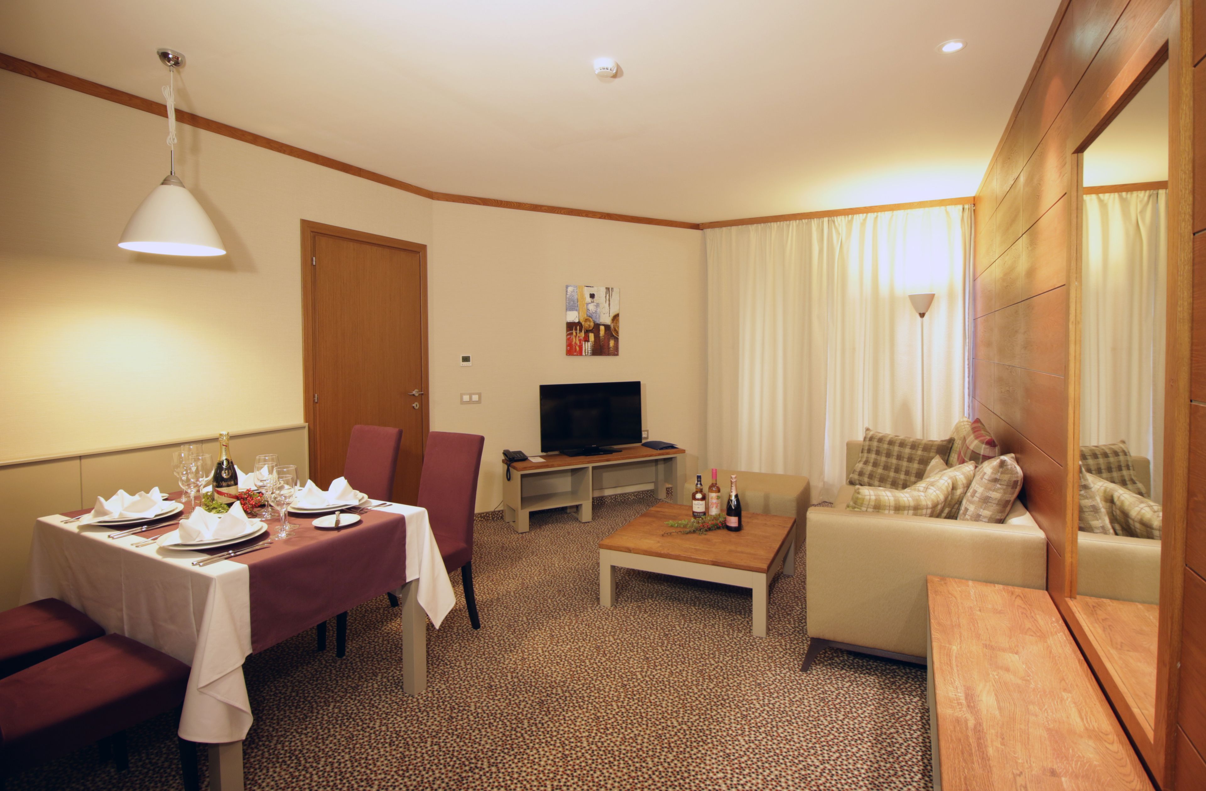 A hotel room with a dining area, a sofa, a television, and a wooden coffee table.