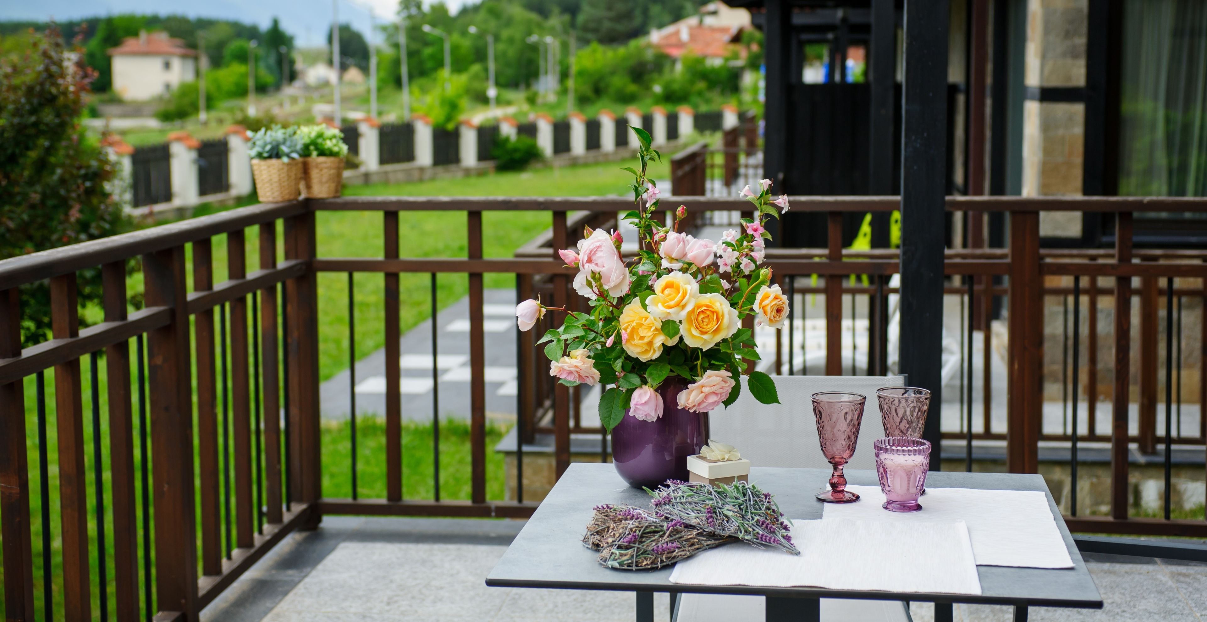 A balcony with a table set for two, featuring a vase of flowers, two glasses, and a small box.