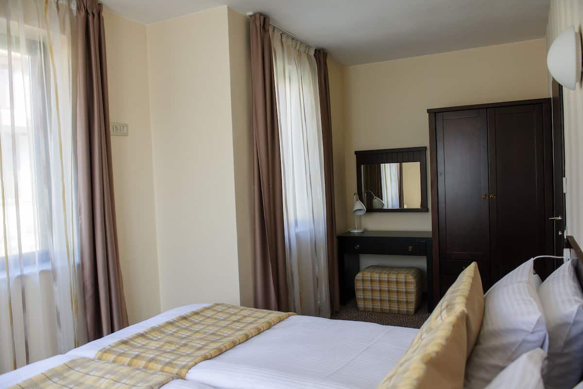 A hotel room with a bed, a desk, a chair, a wardrobe, and a mirror.