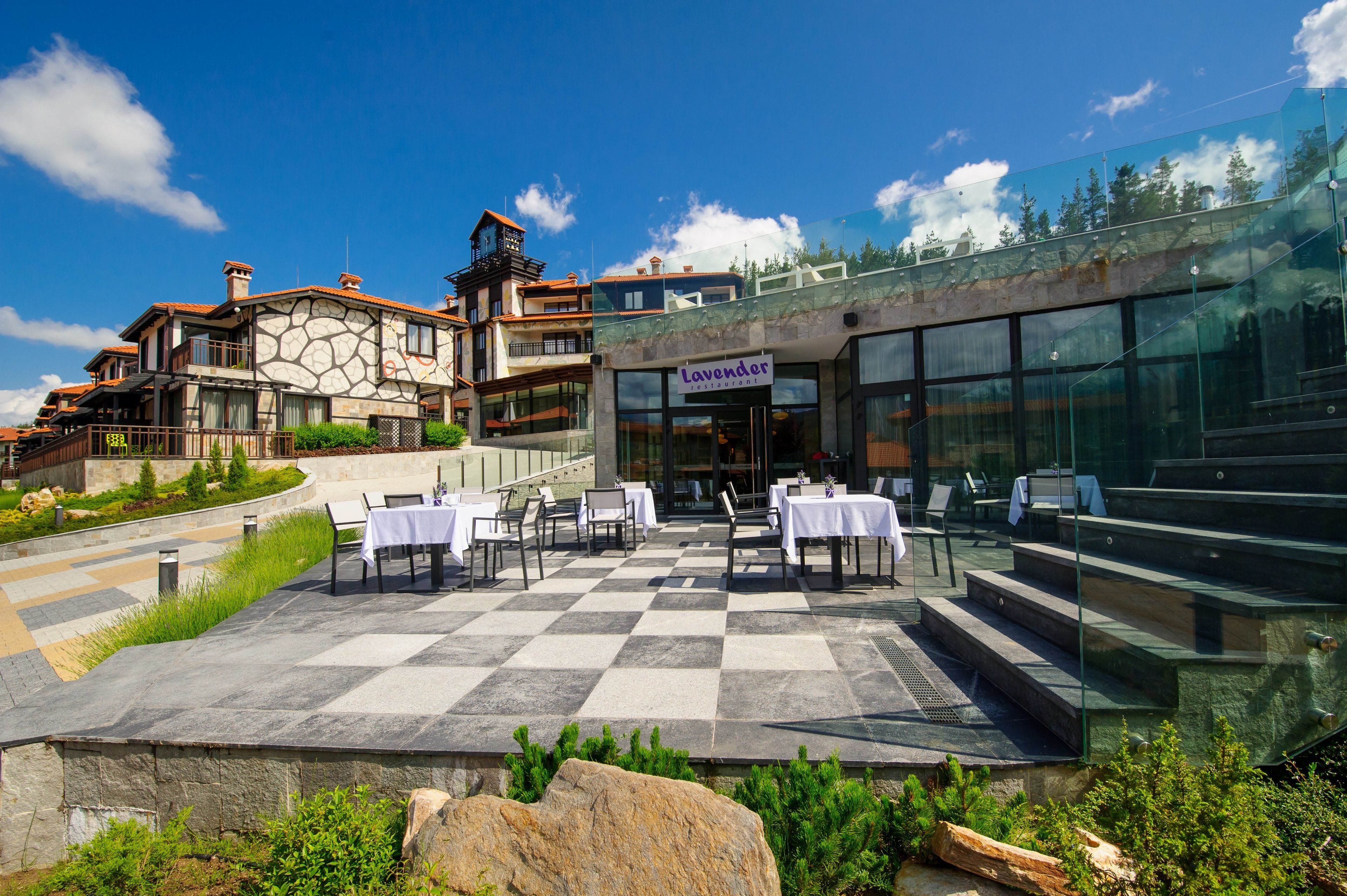 A restaurant with outdoor seating, stone flooring, and a view of a mountain.