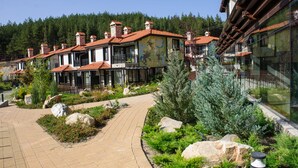 Una hilera de edificios de estilo tradicional con techos de tejas rojas, un sendero pavimentado y jardines ajardinados con rocas y arbustos.