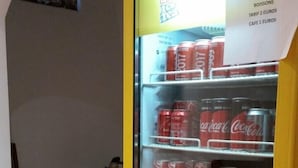 Una máquina expendedora con latas de Coca-Cola y Oasis, un reloj en la pared y un cartel de Boissons.