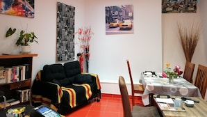 Una sala de estar con sofá, una mesa de comedor con sillas, una estantería y decoración en la pared.