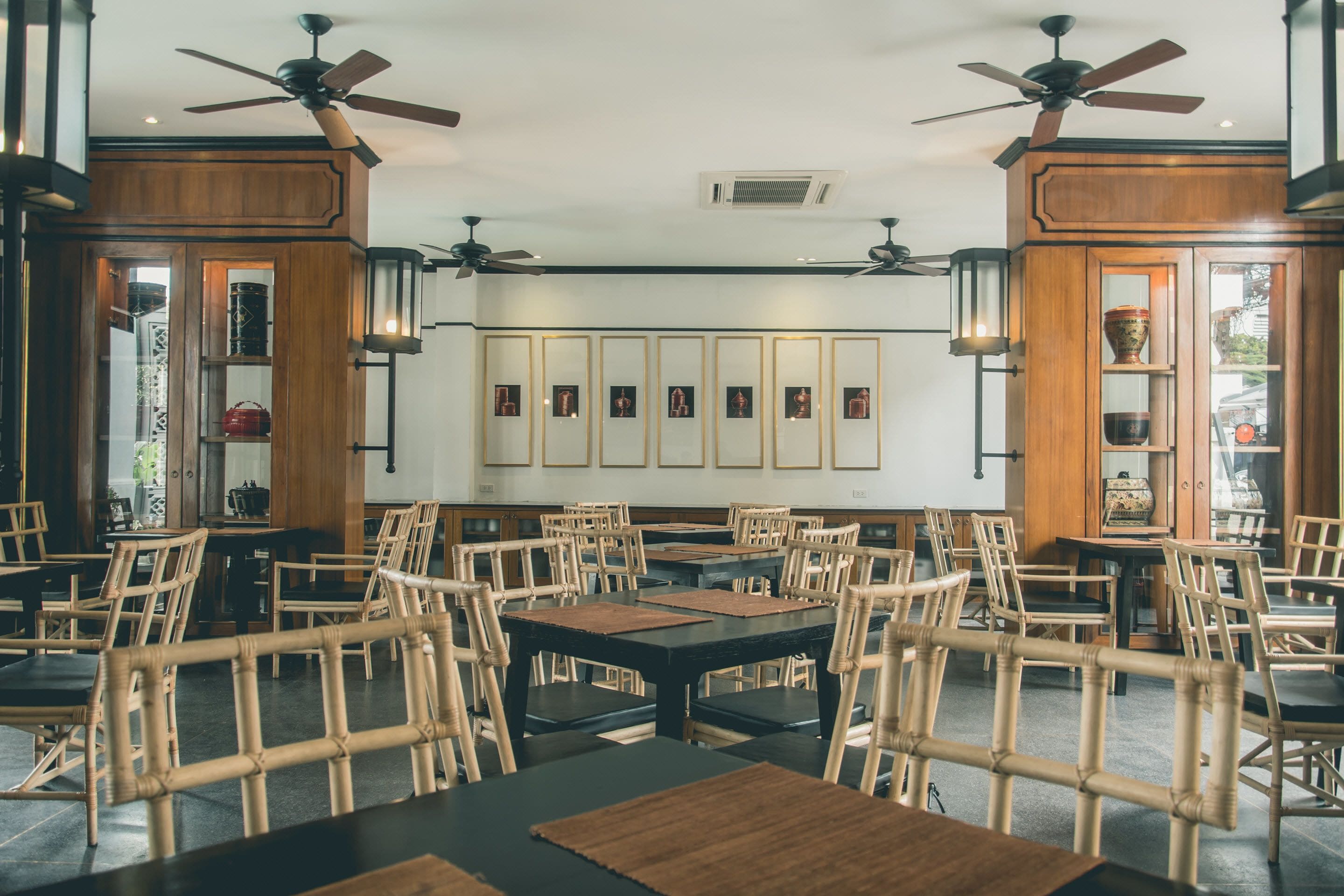 Un restaurant avec des meubles en bois, des ventilateurs de plafond et des tableaux encadrés accrochés aux murs.