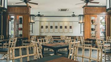 Un restaurant avec des meubles en bois, des ventilateurs de plafond et des tableaux encadrés accrochés aux murs.