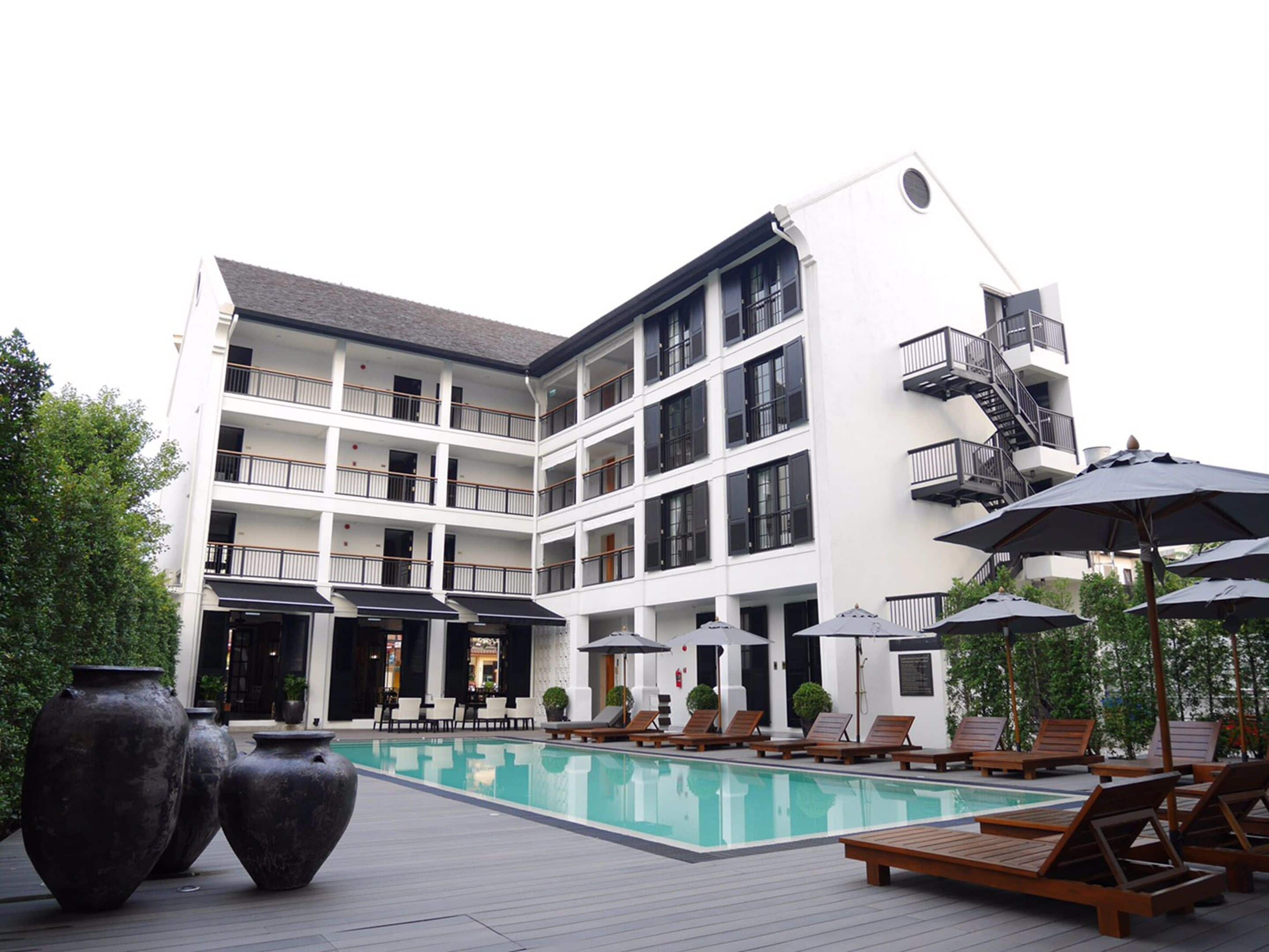 A multi-story hotel with a swimming pool, outdoor seating, and a staircase to the upper floors.