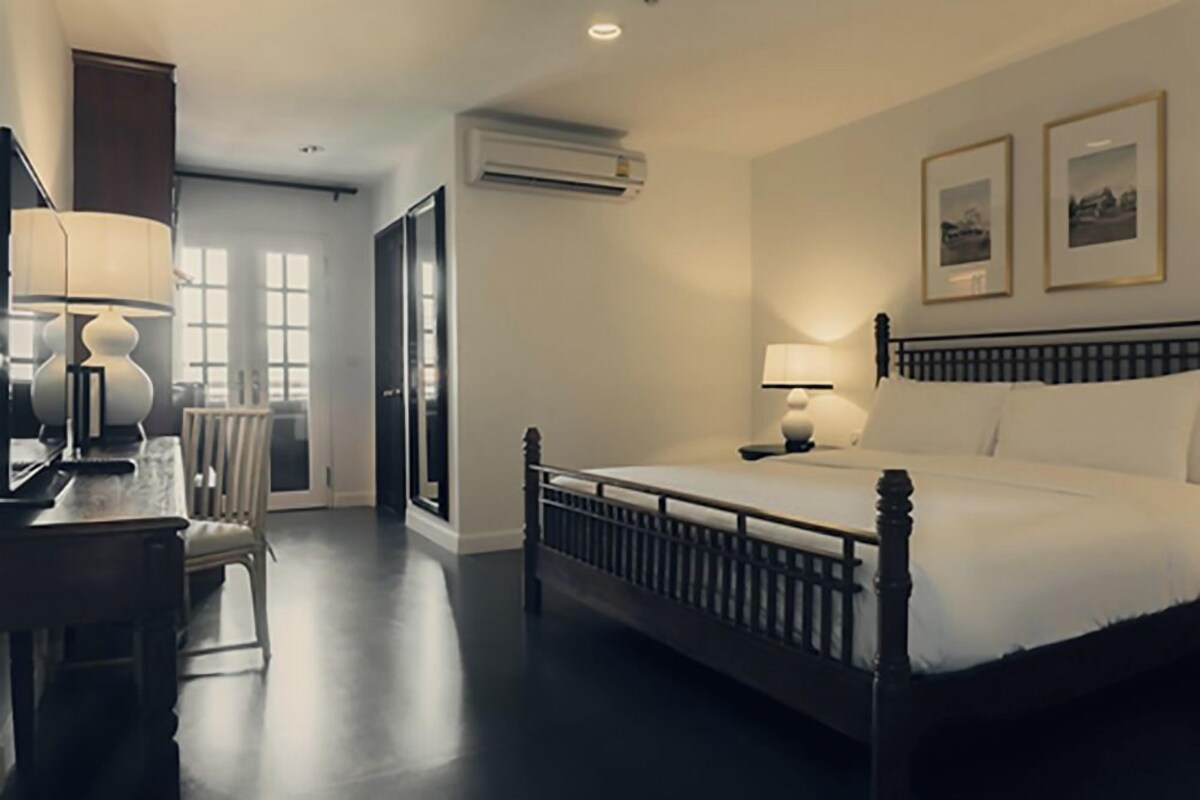 A hotel room with a large bed, bedside lamps, a desk with a lamp, a chair, and a view of the outdoors through a glass door.