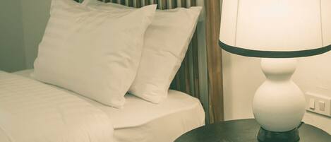 Una cama bien hecha con ropa blanca y almohadas, un cabecero de madera y una mesita de noche con una lámpara blanca.