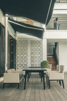 Un patio al aire libre con una mesa y sillas de comedor, un área de estar techada y una escalera que lleva a un nivel superior.