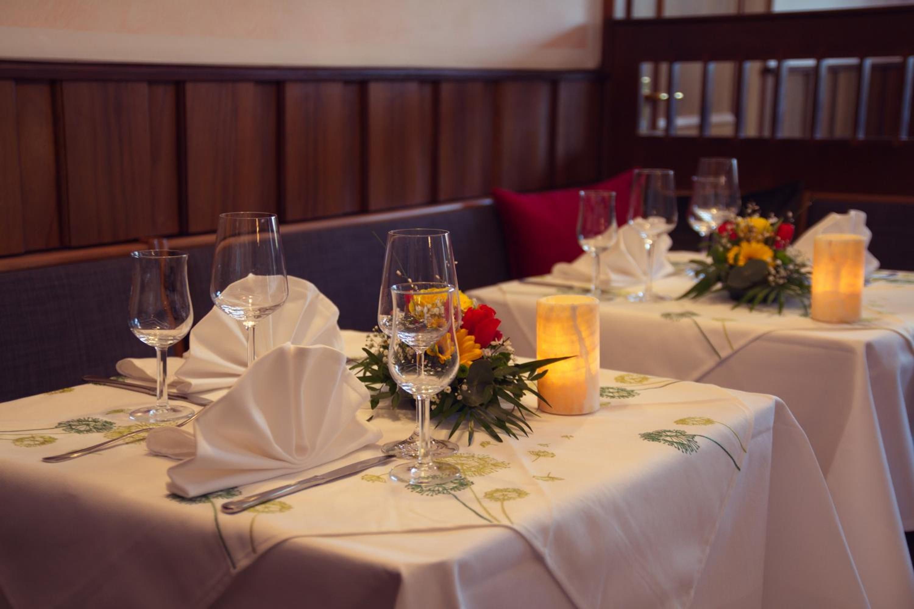 A dining table set with white tablecloths, glassware, and floral centerpieces.