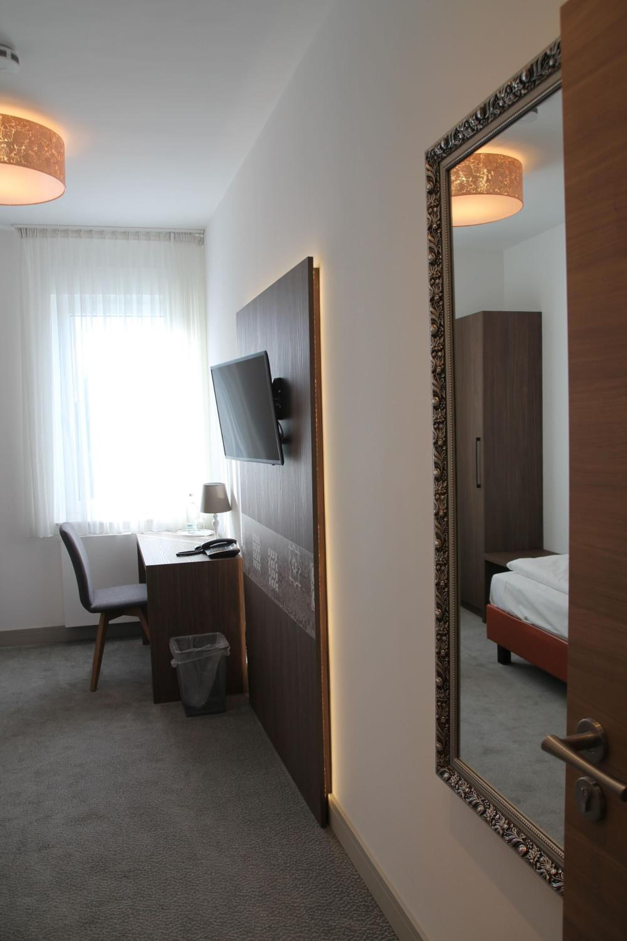 A hotel room with a bed, a desk with a chair, a television, and a large mirror.