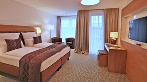 Habitación de hotel con una cama grande, dos sillones, un escritorio con televisor y una ventana con cortinas.