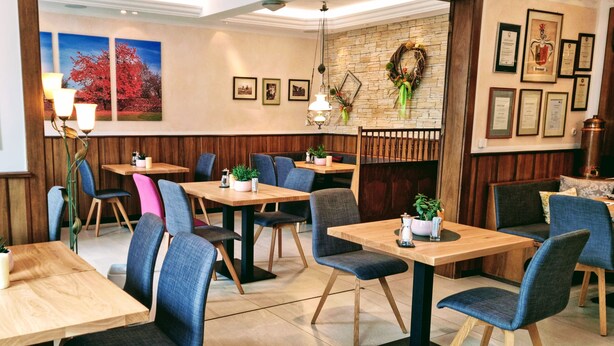 Un restaurante con mesas de madera y sillas azules, cuadros en las paredes y una pared de piedra con un adorno circular.