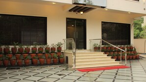 A modern building entrance with a tiled floor, a staircase with a red carpet, and potted plants arranged on either side. - Tulalip Hotel (Gurugram)