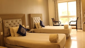 A hotel room with two beds, a nightstand, a chair, and a large window with curtains. - Tulalip Hotel (Gurugram)
