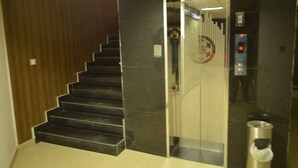 Una escalera que conduce a un ascensor, con barandilla, un bote de basura y una pared con diseño vertical.