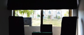 Una habitación con vistas a un edificio con arcos, una ventana con cortina y un portátil sobre una mesita.