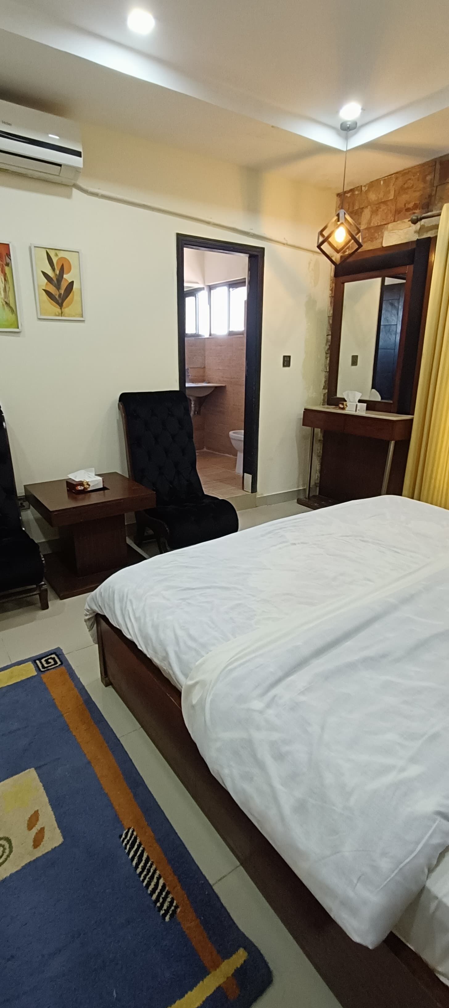 A hotel room with a bed, a desk, a chair, an air conditioning unit, a mirror, and a door leading to a bathroom.
