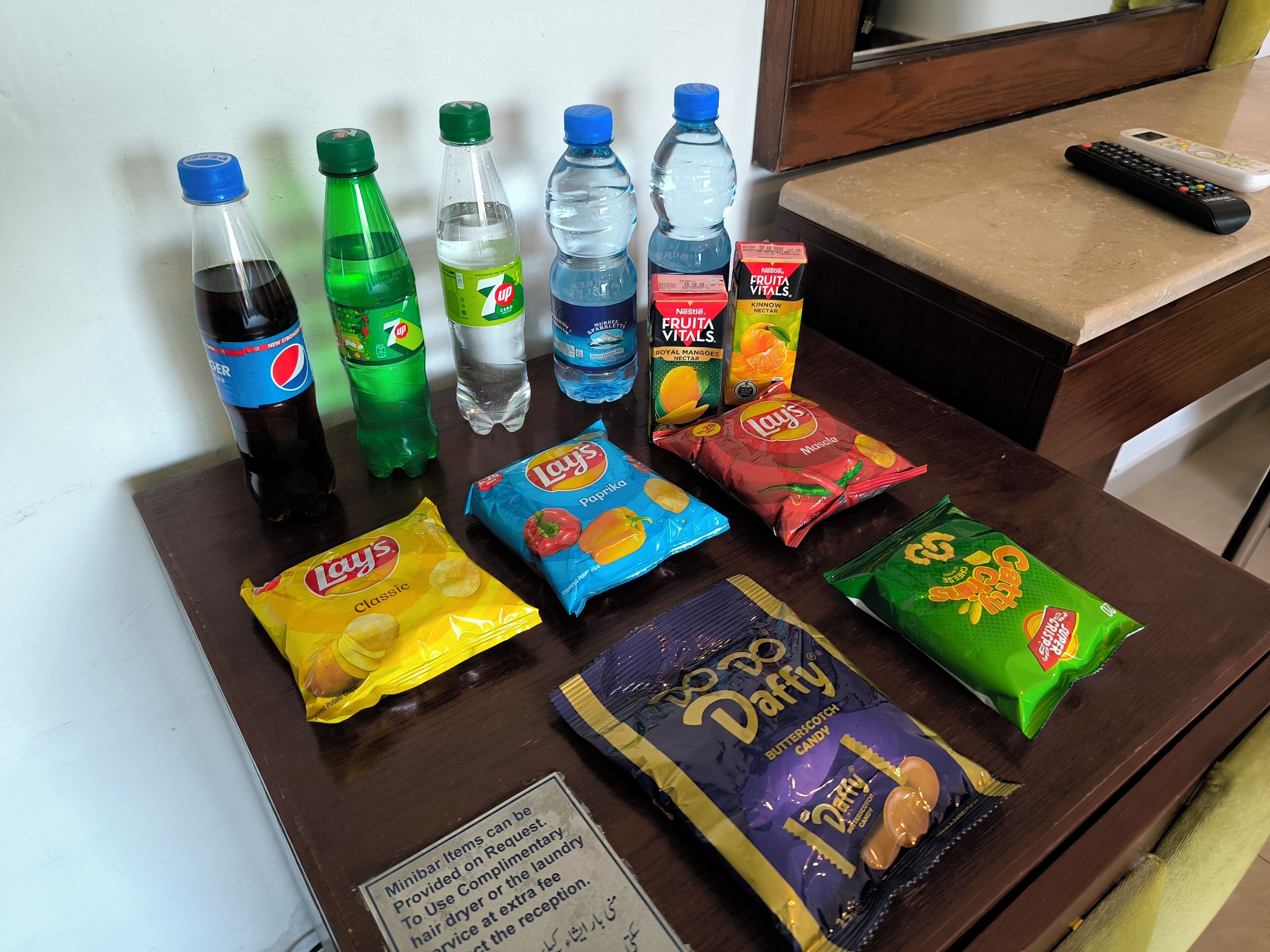 A table with various snacks, drinks, and a remote control.