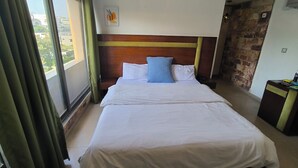 Habitación de hotel con una cama grande, cabecera de madera, vistas por una ventana y pared de piedra.
