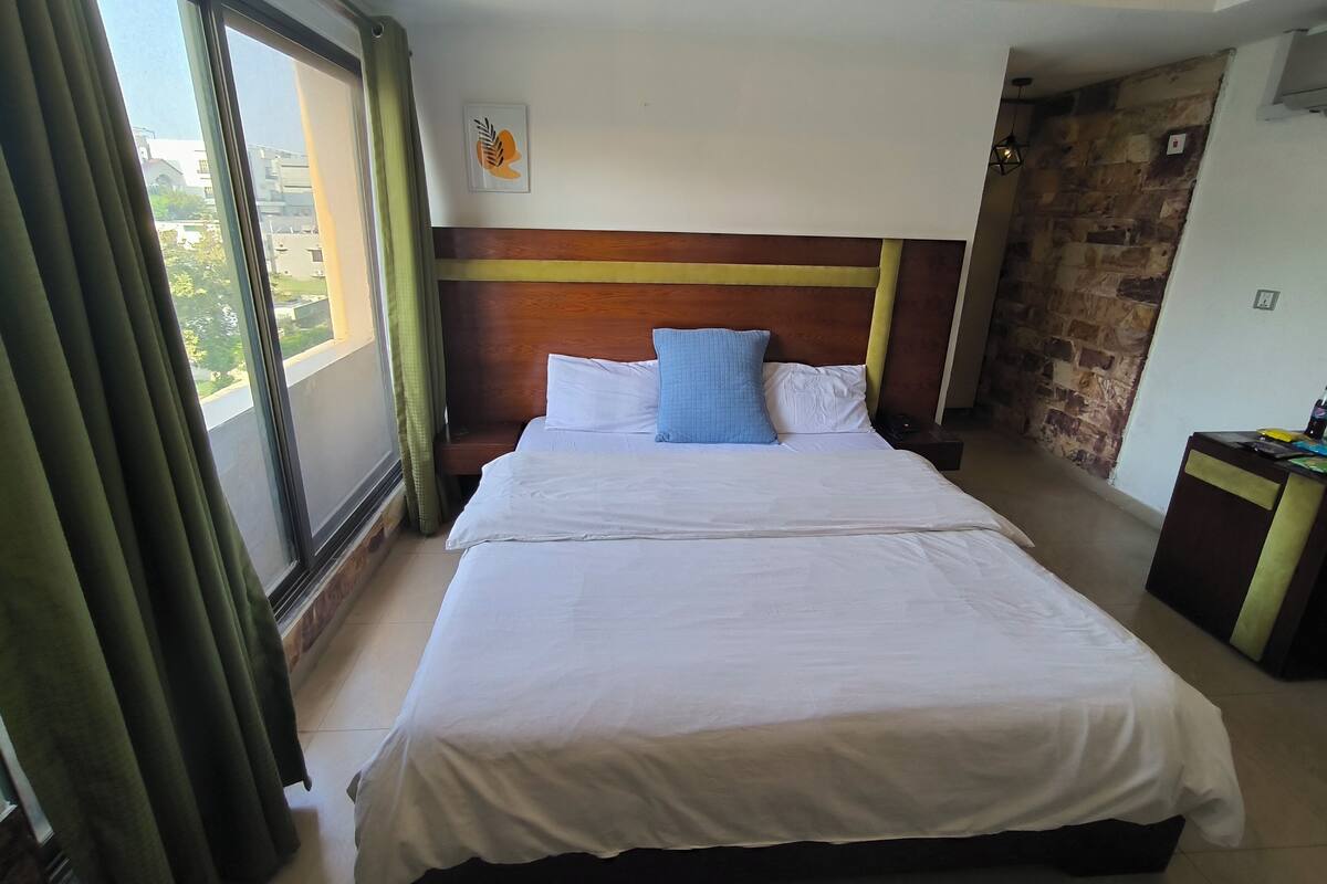 Une chambre d’hôtel avec un grand lit, une tête de lit en bois, une vue par la fenêtre et un mur en pierre.