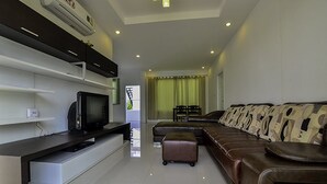 A modern living room with a flat-screen TV, a sofa, and a dining area with a table and chairs. - Baan Taradon By Puppap (Hua Hin)