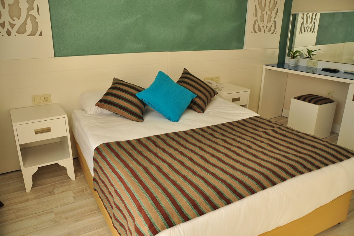 A hotel room with a bed, a nightstand, a desk, and a mirror.